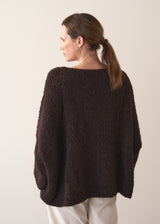 Woman wearing a dark brown boucle sweater and cream trousers against a plain background