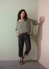 Woman wearing a boucle light green sweater and dark jeans against a plain background
