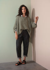 Woman wearing a boucle light green sweater and dark jeans against a plain background