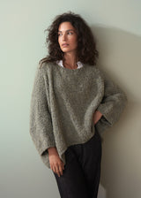 Woman wearing a boucle light green sweater and dark jeans against a plain background
