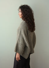 Woman wearing a boucle light green sweater and dark jeans against a plain background