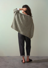 Woman wearing a boucle light green sweater and dark jeans against a plain background