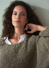 Woman wearing a boucle light green sweater and dark jeans against a plain background