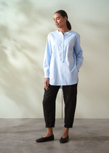 Woman wearing a light blue shirt and black trousers against a neutral background