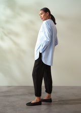 Woman wearing a light blue shirt and black trousers against a neutral background