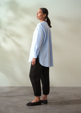 Woman wearing a light blue shirt and black pants against a neutral background