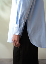 Light blue shirt with rolled-up sleeves worn by a person against a neutral background