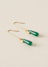 Gold earrings with green teardrop-shaped stones on a beige background