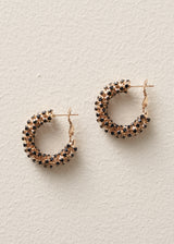 A pair of small hoop earrings with a rose gold base covered in black and clear rhinestones, displayed on a textured off-white background.