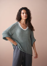 Woman wearing a green knit sweater and plaid linen trousers against a beige background