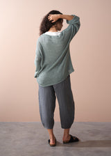 Woman wearing a green sweater and checkered linen trousers against a beige background