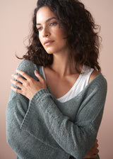 Woman wearing a green knitted cardigan over a white top against a beige background