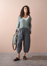 Woman wearing a green sweater and checkered linen trousers, holding a green bag against a beige background