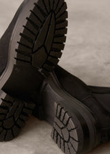 Close-up of black boots with tread pattern on a neutral background