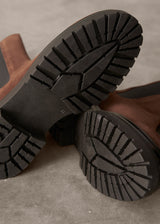 Close-up of brown suede boots with black soles on a gray surface