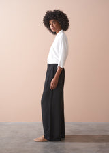 Woman wearing a white blouse and black wide-leg trousers against a beige background