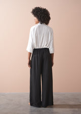 Person wearing a white shirt and black wide-leg trousers against a beige background