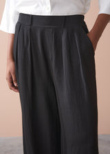 Black wide-leg trousers worn with a white shirt against a beige background