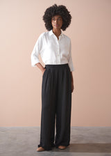 Woman wearing a white shirt and black wide leg trousers against a beige background