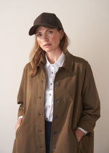Woman wearing a brown coat and cap against a plain background