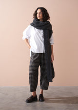 Woman wearing a white shirt, black checkered pants, and a dark scarf against a beige background