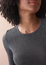 Woman wearing a silver metallic long sleeve top against a beige background