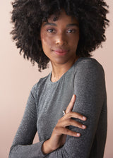 Woman wearing a silver metallic long sleeve top against a beige background