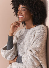 Woman wearing a silver metallic long sleeve top against a beige background