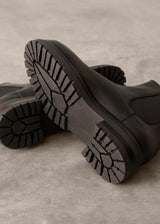 Close-up of black rubber boots with tread pattern on a beige background