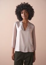 Woman wearing a pale lilac satin blouse against a beige background