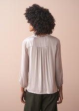 Person wearing a pale lilac satin blouse with long sleeves against a beige background