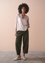 Woman wearing a pale lilac satin blouse and green pants against a beige background