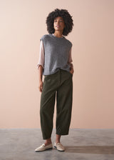 Woman wearing a gray sleeveless top and green pants against a beige background