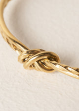 Gold bracelet with a knot design on a light beige background
