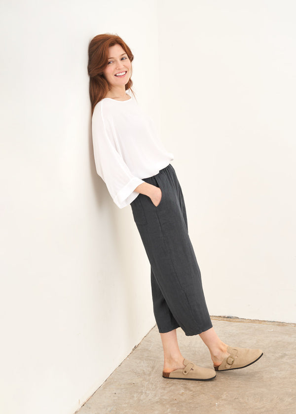 A model wearing a white long sleeve top with dark grey cropped linen trousers and taupe coloured clogs