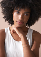 Woman wearing a white tank top with visible jewelry against a beige background