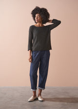 Woman wearing a striped gold and black top against a beige background