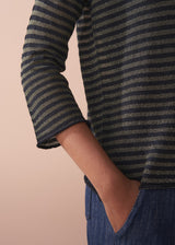 Woman wearing a striped gold and black top against a beige background