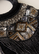 Close-up detail of a black beaded garment featuring geometric patterns of metallic silver, bronze, and gold sequins and beads.