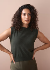 Woman wearing a dark green sleeveless top against a beige background