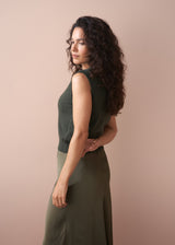 Woman wearing a green sleeveless top and green skirt against a beige background