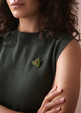Person wearing a dark green sleeveless top with a heart-shaped brooch on a neutral background