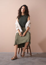 Woman sitting on a chair wearing a green dress and white cardigan against a beige background