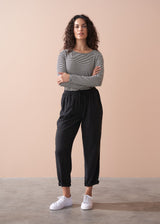 Woman wearing a striped long sleeve shirt and black drawstring trousers against a beige background