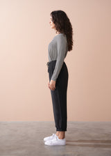 Woman wearing a striped long sleeve shirt and black drawstring trousers against a beige background