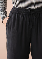 Woman wearing a striped long sleeve shirt and black drawstring trousers against a beige background