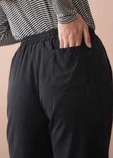 Woman wearing a striped long sleeve shirt and black drawstring trousers against a beige background