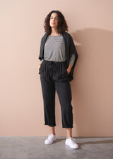 Woman wearing a striped long sleeve shirt and black drawstring trousers against a beige background