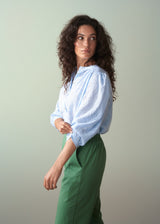 Woman wearing a light blue blouse and green trousers against a plain background