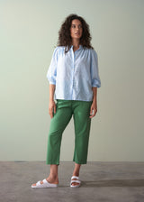 Woman wearing a light blue shirt and green trousers against a plain background